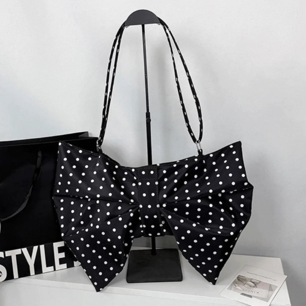 Black pleated bow crossbody tote bag displayed on a stand against a white background.