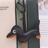 A black dachshund leather keychain charm attached to a green and beige bag.