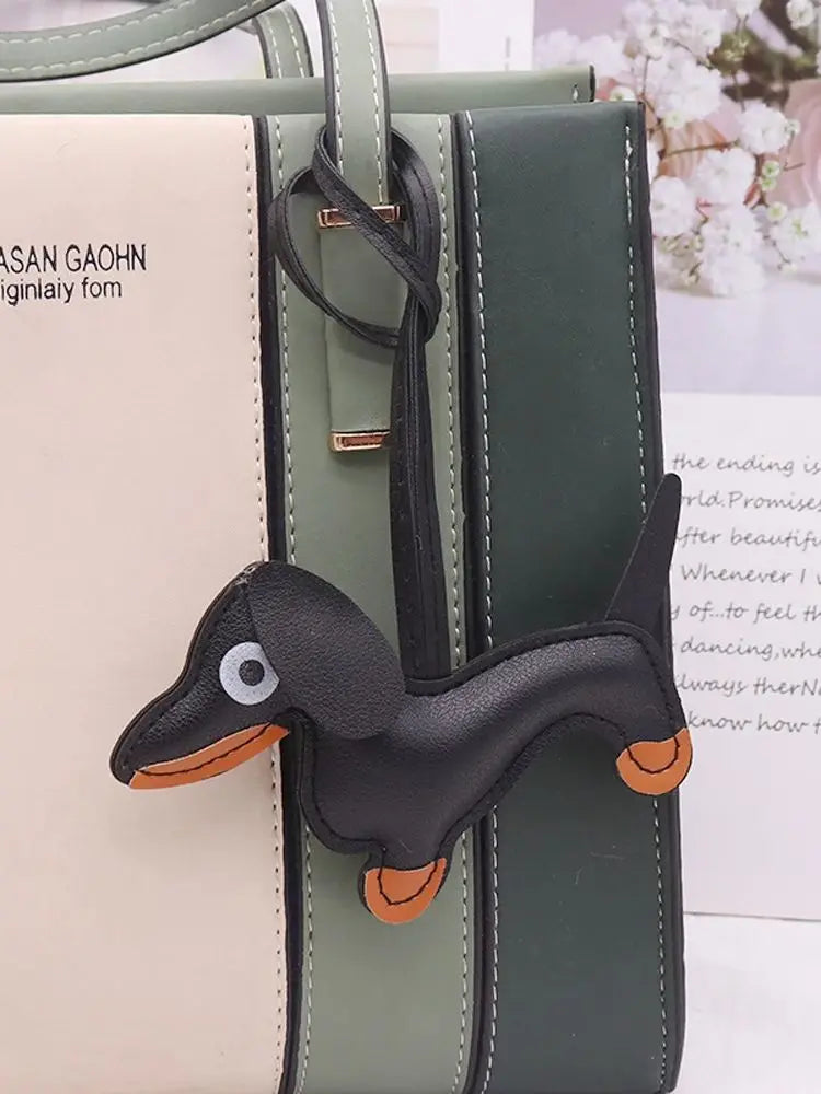 A black dachshund leather keychain charm attached to a green and beige bag.