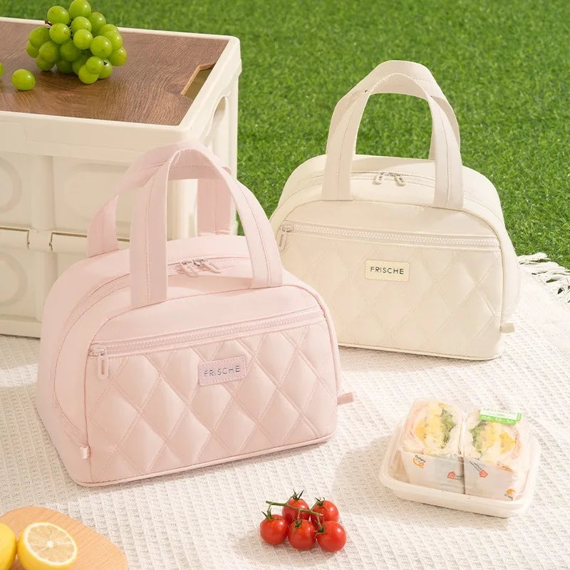 A pink quilted insulated lunch tote bag next to a cream-colored bag and fresh fruit on a white surface.