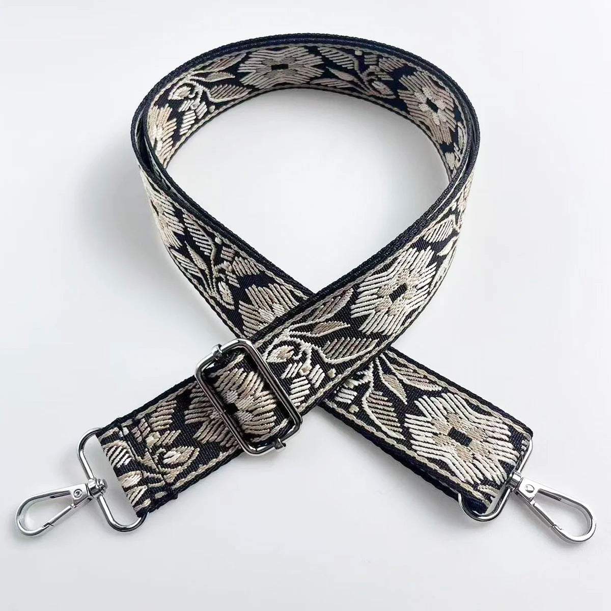 A black and beige patterned jacquard strap for a crossbody bag, shown crossed.