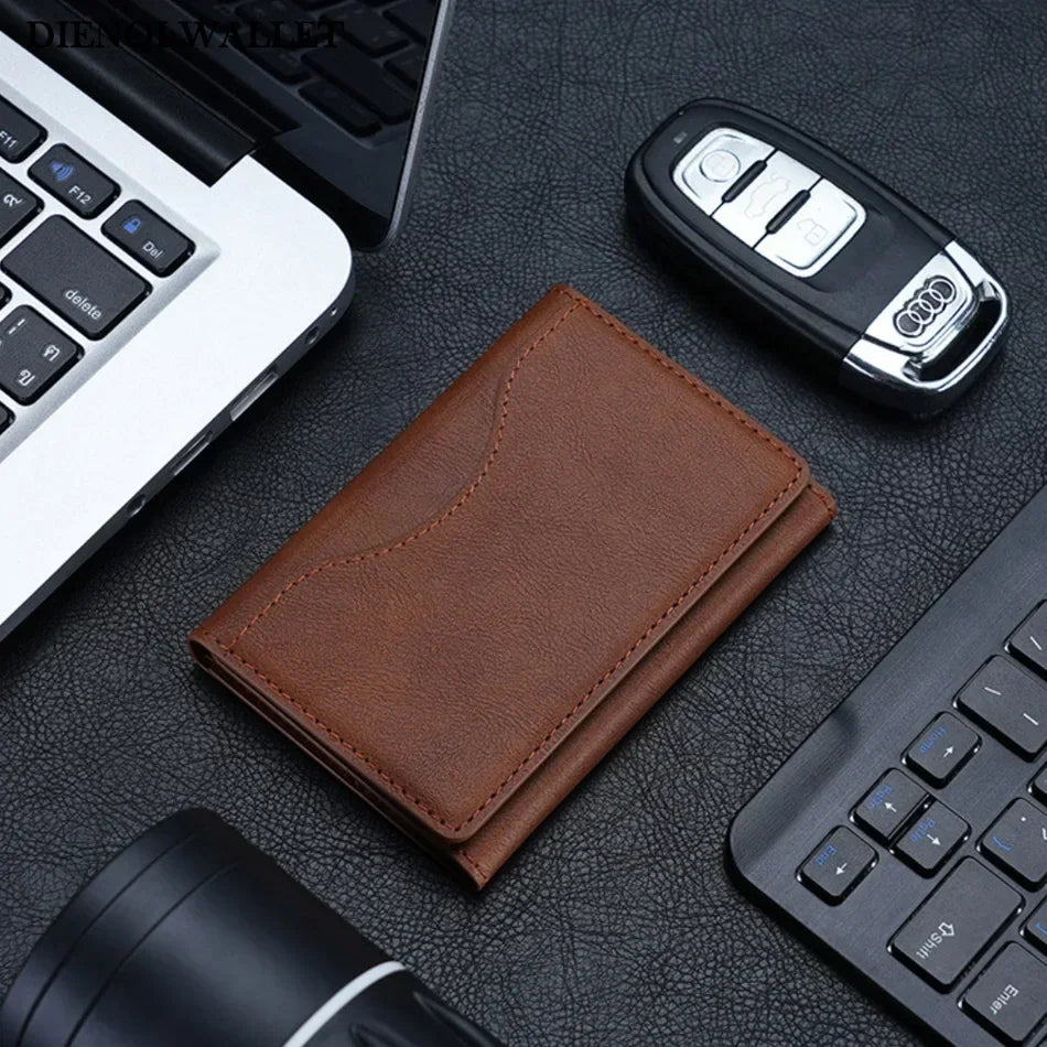 A brown magnetic leather card wallet is shown next to a laptop and a black electronic device on a dark surface.