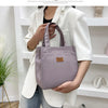 A person holds a mauve aluminum foil insulated lunch bag in a white blazer against a white shelf background.