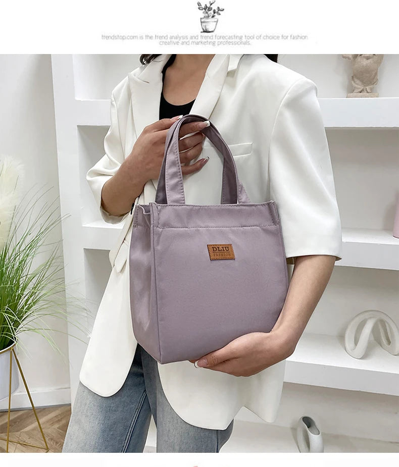A person holds a mauve aluminum foil insulated lunch bag in a white blazer against a white shelf background.