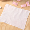Une serviette faciale en coton blanche et compressée est posée sur une surface en bois avec plusieurs tampons roses comprimés