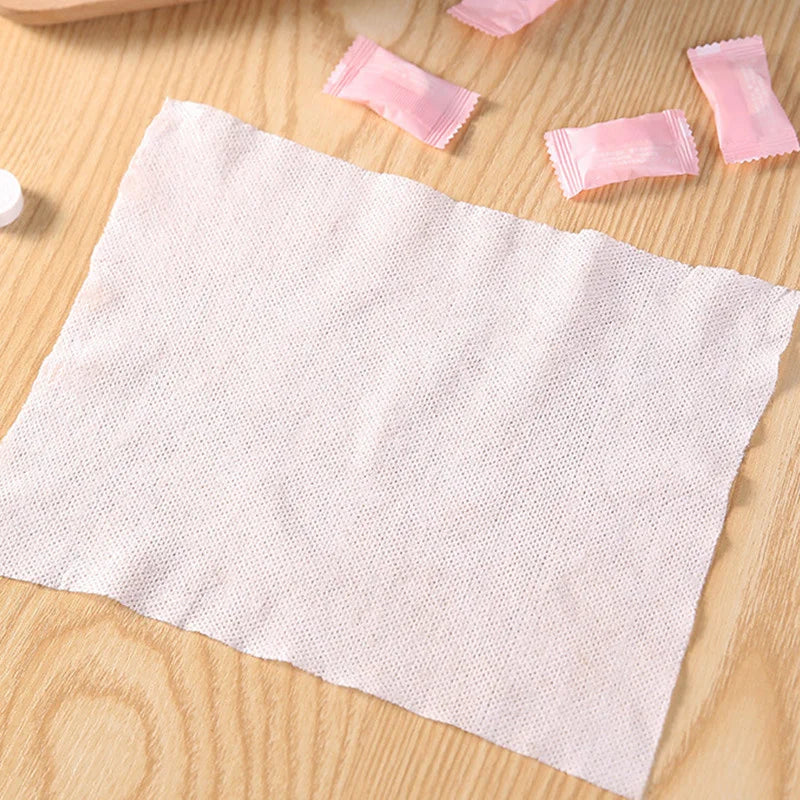 Une serviette faciale en coton blanche et compressée est posée sur une surface en bois avec plusieurs tampons roses comprimés