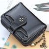 A black PU leather compact wallet with a zipper and gold chain resting on a white box.