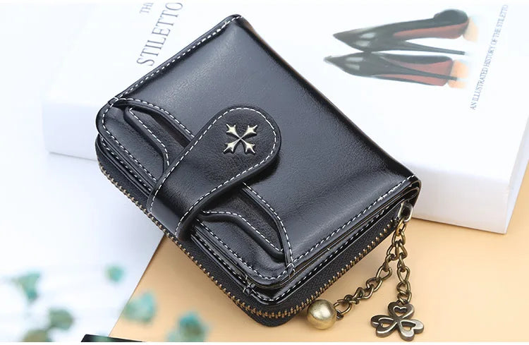 A black PU leather compact wallet with a zipper and gold chain resting on a white box.