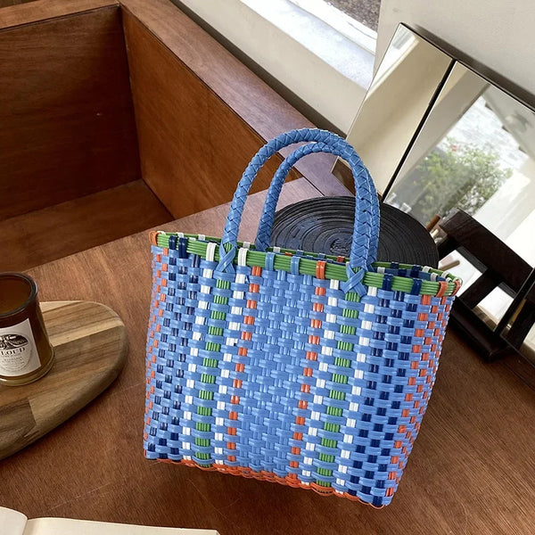 Una bolsa de mimbre de PVC para vegetales con rayas azules, naranjas y verdes sobre una superficie de madera.