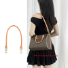A woman is holding a brown leather shoulder bag with a genuine Vachetta strap.
