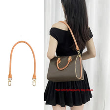 A woman is holding a brown leather shoulder bag with a genuine Vachetta strap.
