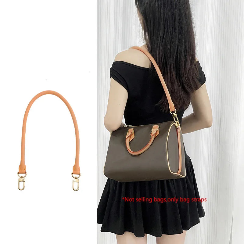 A woman is holding a brown leather shoulder bag with a genuine Vachetta strap.