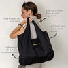 A woman holds a black foldable mini keychain tote bag, demonstrating its long handles and durability.