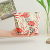 A hand holds a floral canvas makeup bag featuring red and green flowers with the text DIDF BAG printed on it.