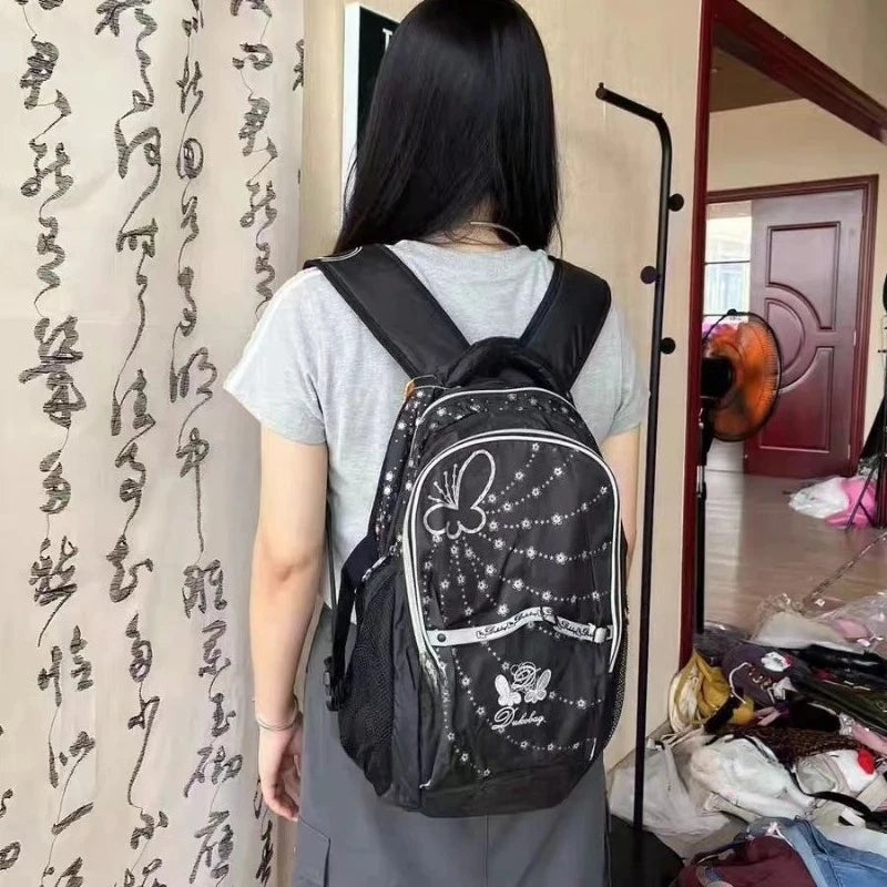 A person is shown from the back wearing a black backpack with a butterfly print and a gray t-shirt.