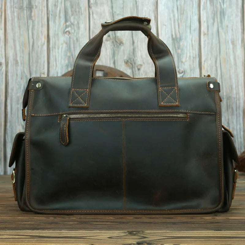 A dark brown genuine cowhide leather briefcase with leather handles and stitching set against a wooden background.