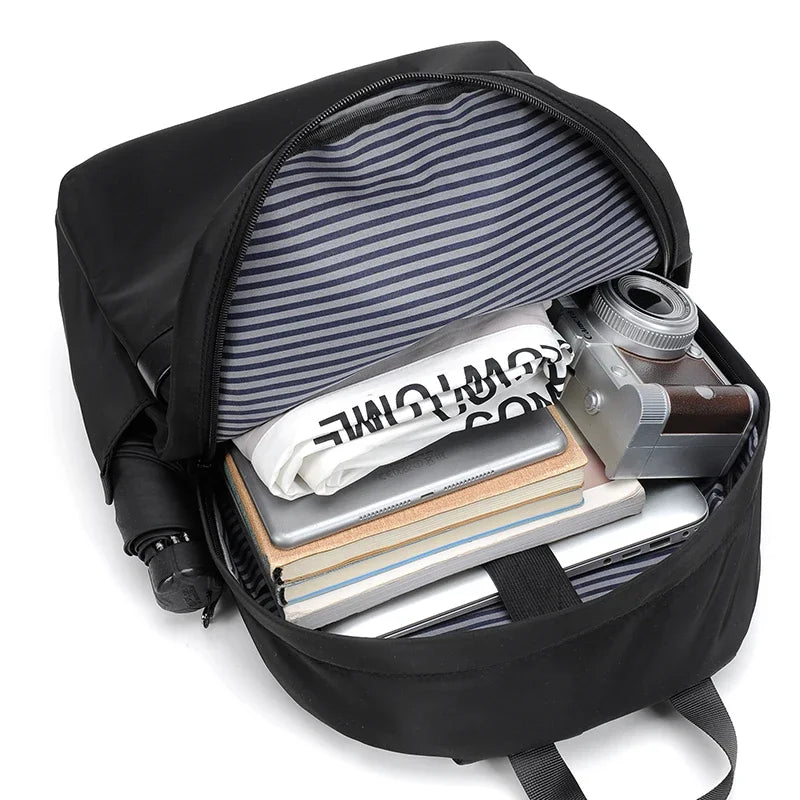 A black laptop backpack is open, showing a padded sleeve containing a camera and several notebooks.