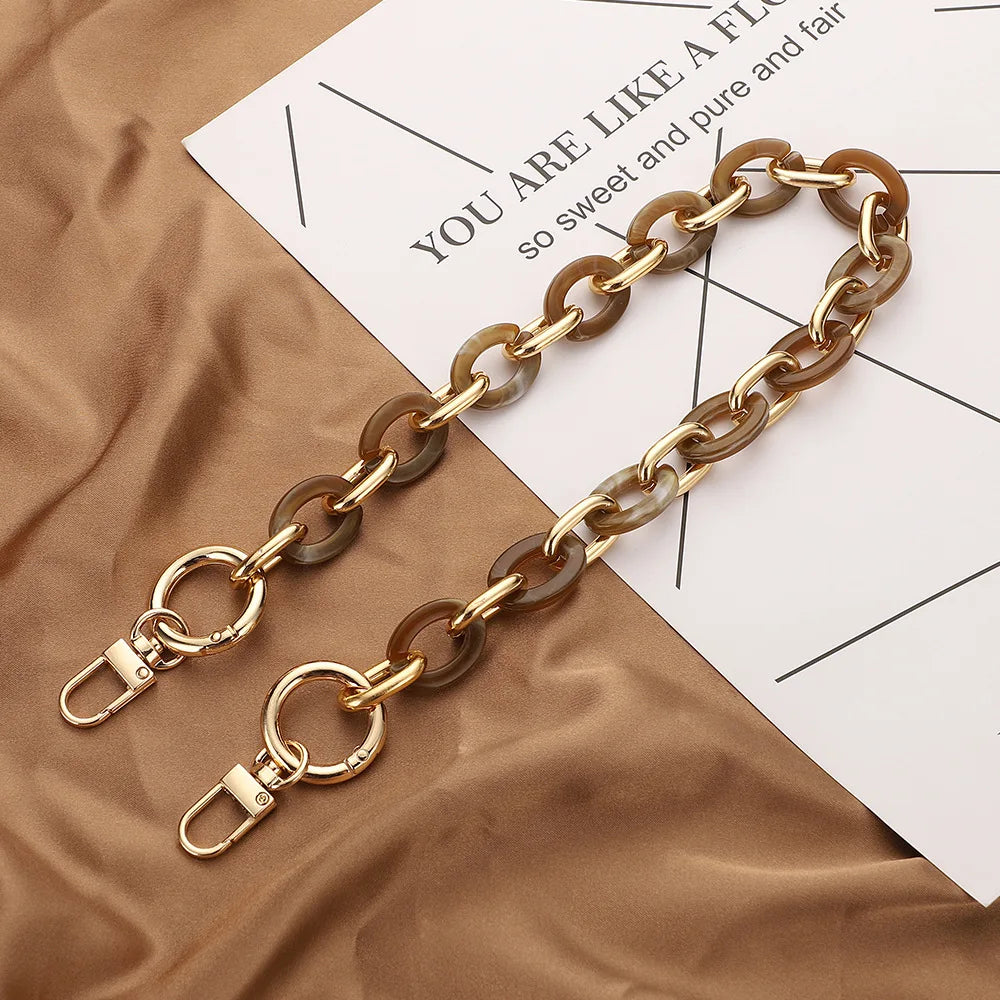 A gold-toned acrylic handbag strap chain laid across a piece of paper on brown fabric.