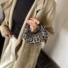 A woman holds a black leopard print PU leather mini tote handbag under a beige trench coat.