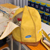A yellow banana-shaped backpack with a zipper and brown trim is shown on a wooden surface.