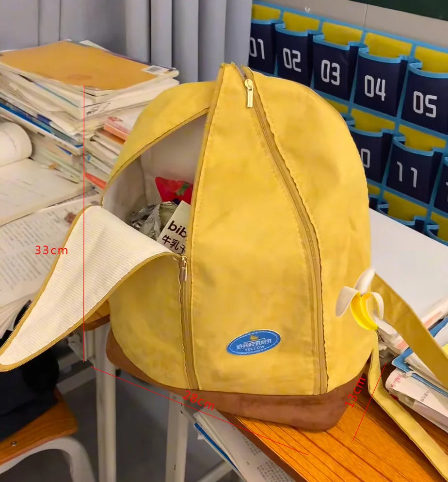 A yellow banana-shaped backpack with a zipper and brown trim is shown on a wooden surface.