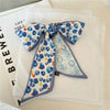 Foulard de cheveux en soie floral bleu et blanc noué en nœud, exposé sur un tissu blanc.