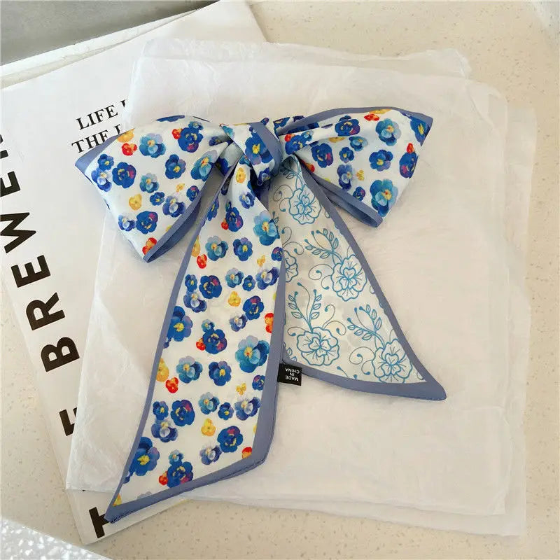 Foulard de cheveux en soie floral bleu et blanc noué en nœud, exposé sur un tissu blanc.