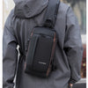 A man wearing a gray jacket is carrying a black anti-theft zippered crossbody bag on his back.