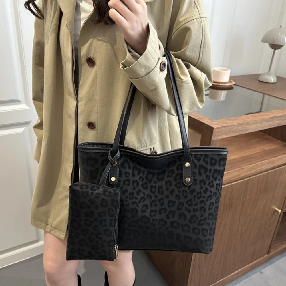 A woman holds a black leopard print tote bag with a leather strap against a light beige jacket.