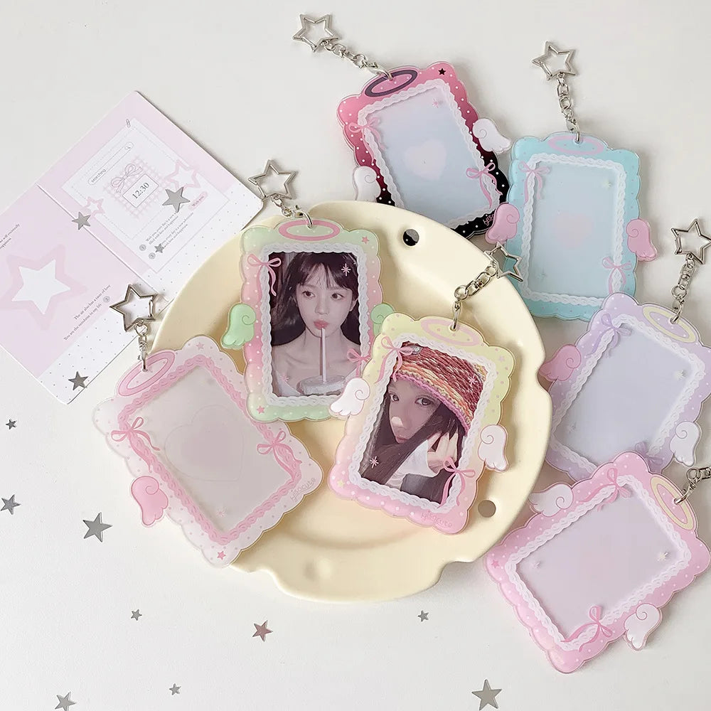 A set of pink and blue angel wings photocard holders with clear display cases and silver chains on a white background.