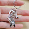 Silver keychain set featuring a cowboy boot, hat, and horseshoe charms held by a hand.