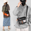 A person is holding a black waterproof nylon crossbody bag against a gray hooded jacket.