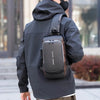 A person wearing a black jacket is carrying a dark gray anti-theft crossbody chest bag on their back.