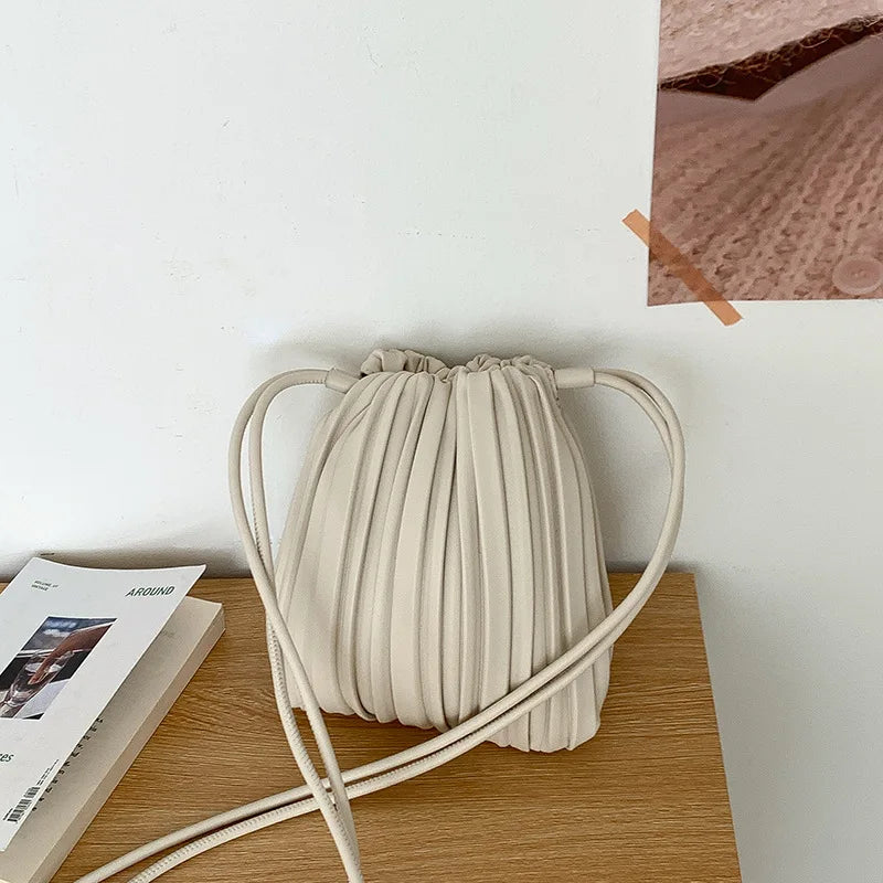 A beige PU leather pleated crossbody bag resting on a wooden surface.