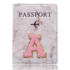 Portada de pasaporte de cuero marmolado rosa con inicial A dorada y símbolo de avión.