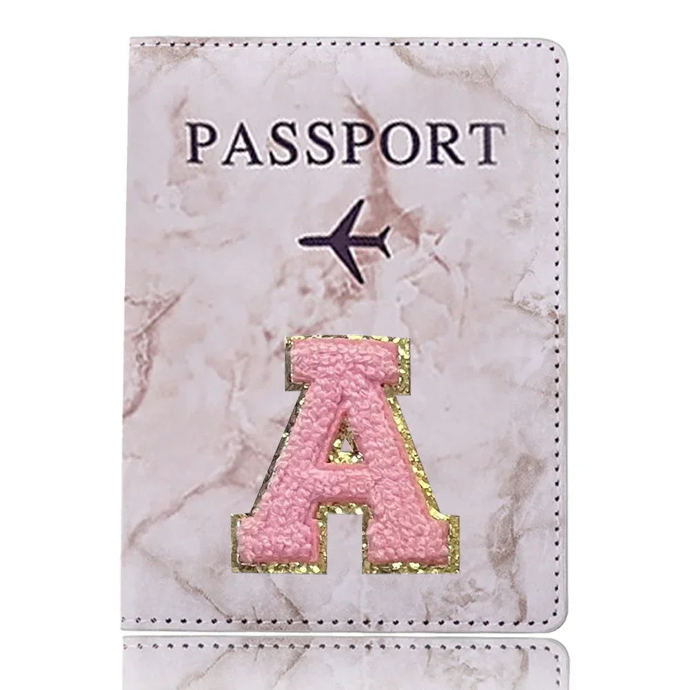 Portada de pasaporte de cuero marmolado rosa con inicial A dorada y símbolo de avión.