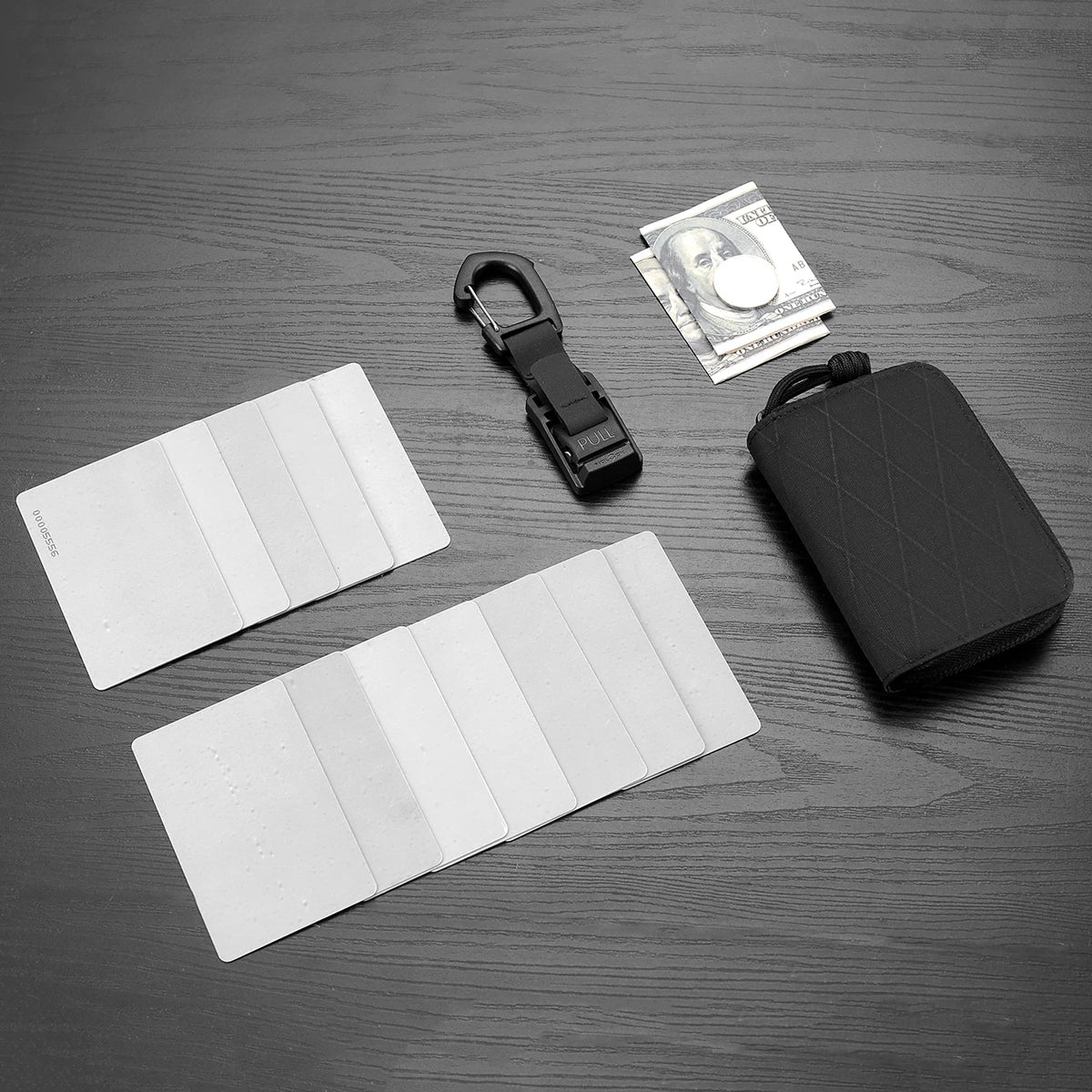 A black RFID zipper wallet is shown next to a stack of US dollar bills and several white plastic cards on a dark surface.