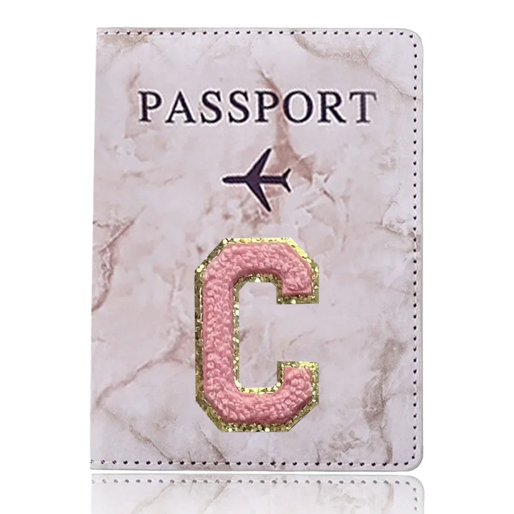 Portafolio de pasaporte de cuero marmolado rosa con inicial C dorada e icono de avión.