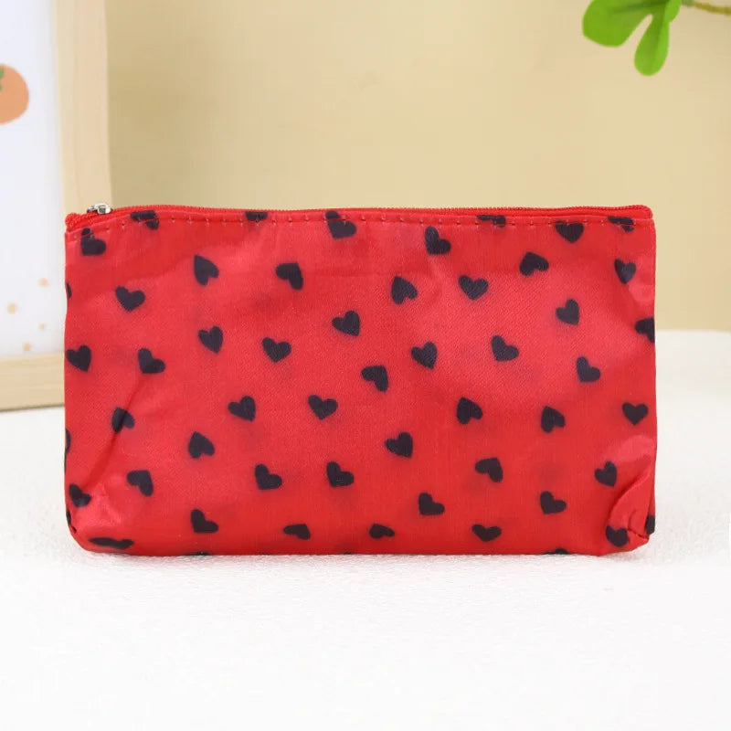 A red cosmetic bag with a leopard print pattern and a zipper, lying on a white surface.
