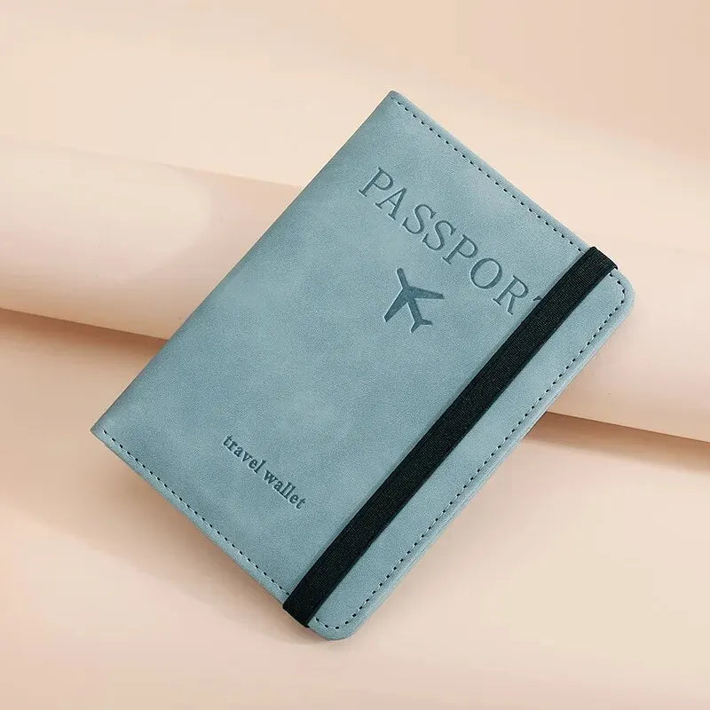 A light blue passport wallet with a black trim and a silver airplane icon is shown on a beige surface.