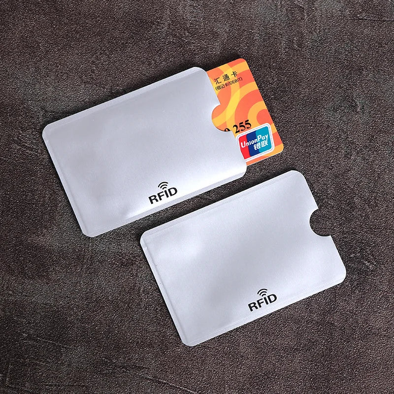 Two clear plastic anti-scan card sleeves for credit cards and RFID protection are displayed on a dark surface.