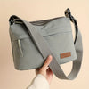 A gray nylon crossbody shoulder bag with multiple zippered compartments is held by a hand.