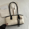 A beige leather tote bag with black handles and gold hardware resting on a white textured surface.