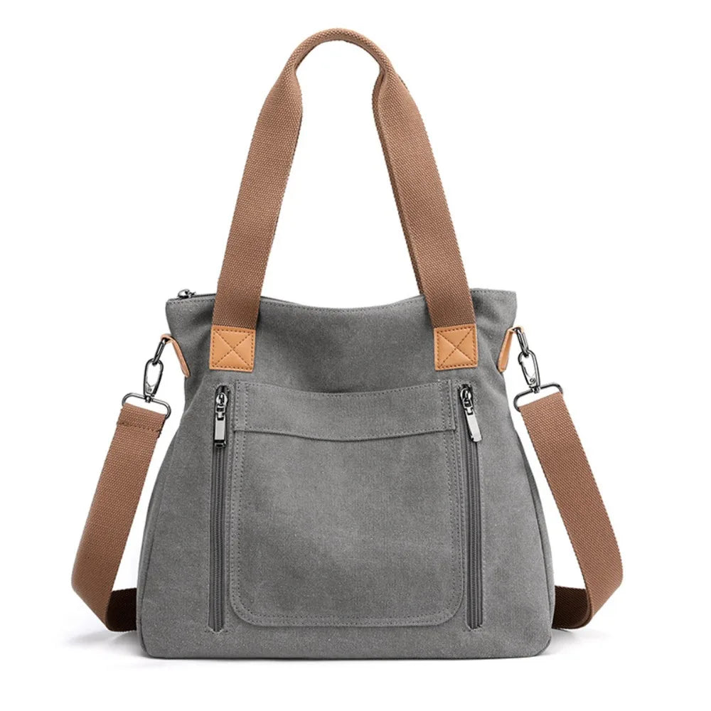 A gray canvas tote bag with brown leather straps and pockets shown from the front.