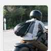 A person wearing a black helmet with a backpack is sitting on a motorcycle in an outdoor setting.