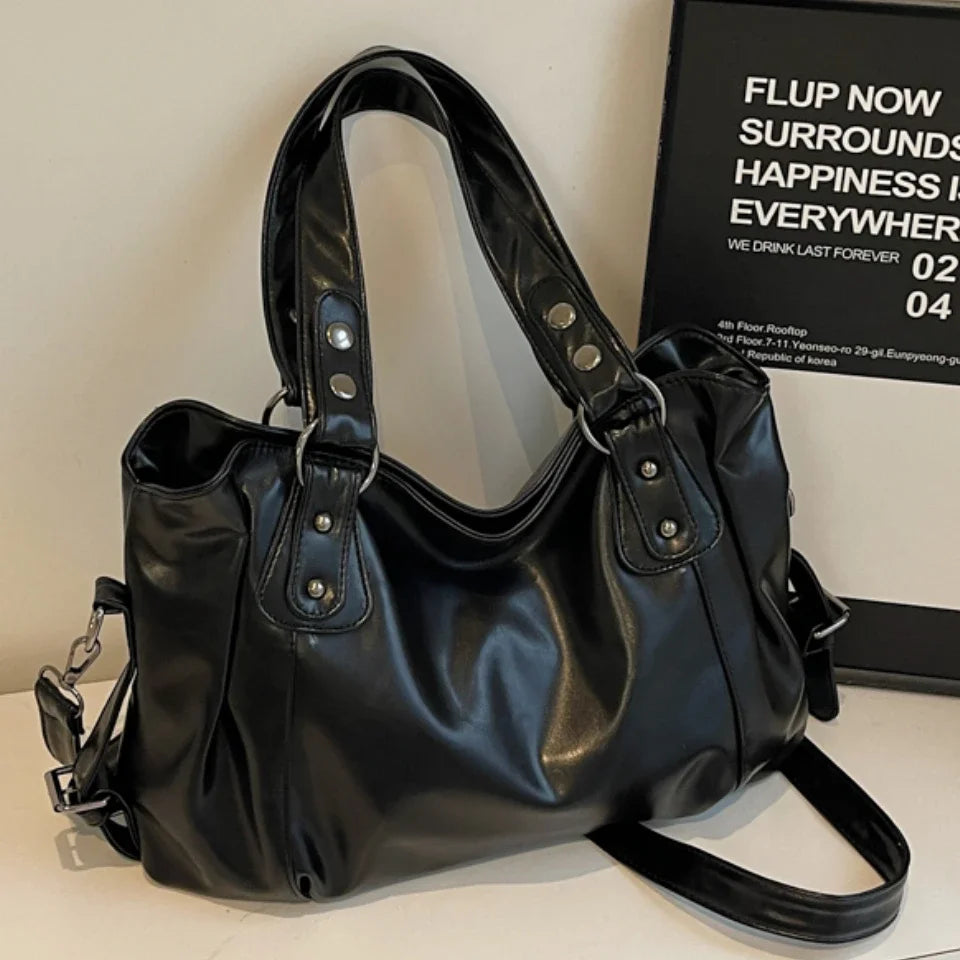 A black vintage style leather tote bag with a crossbody strap is displayed on a white surface.