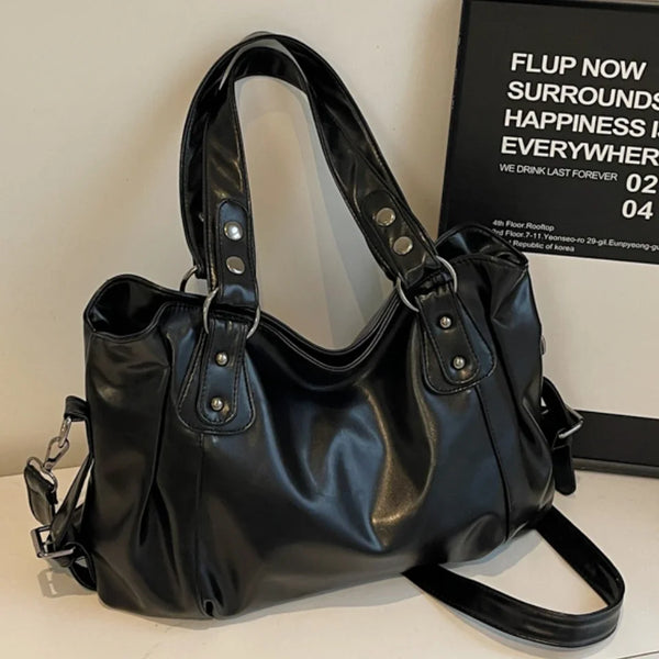 A black vintage style leather tote bag with a crossbody strap is displayed on a white surface.