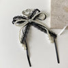 A black lace bow with white pearls and a heart charm attached to a black cord.