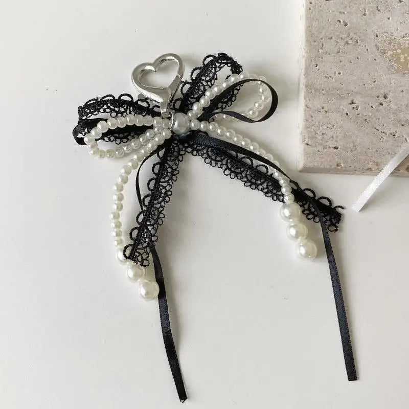 A black lace bow with white pearls and a heart charm attached to a black cord.