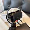 A black leather shoulder bag with gold hardware resting on a white blanket next to a dark leather sofa.